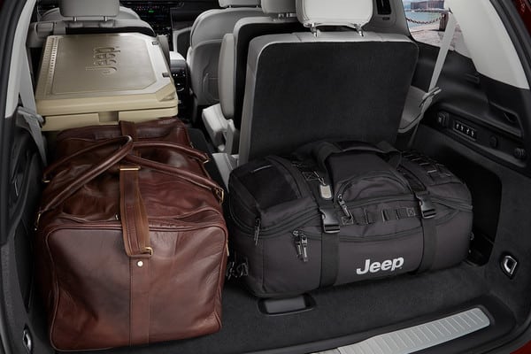 Luggage space in a Jeep vehicle with brown leather and black duffel bags and a tan cooler.