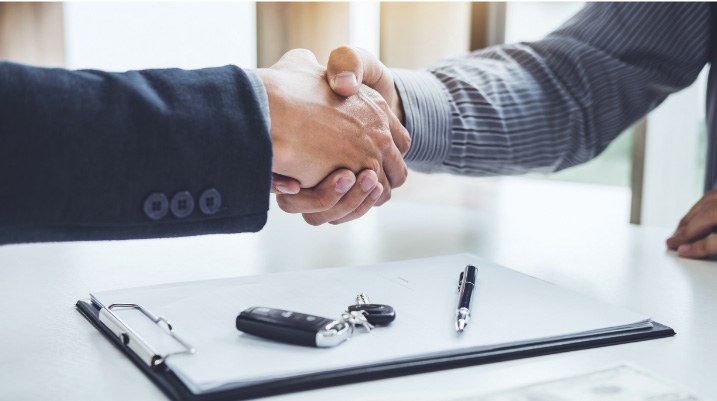 Deux personnes se serrent la main après la conclusion d'un contrat, avec des clés de voiture et un stylo sur la table.