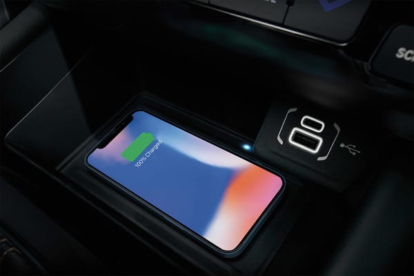 Smartphone wirelessly charging in a car, showing 100% battery on screen.