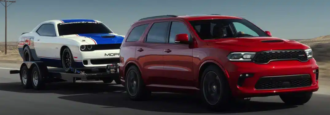 Véhicule SUV rouge tractant une voiture de course blanche sur une remorque, roulant sur une route dégagée.