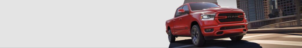 Red RAM pickup truck driving on an urban road with city buildings in the background.