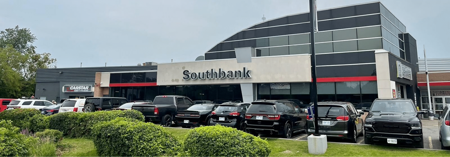 Car dealership with sign reading "Southbank" surrounded by parked cars and greenery.