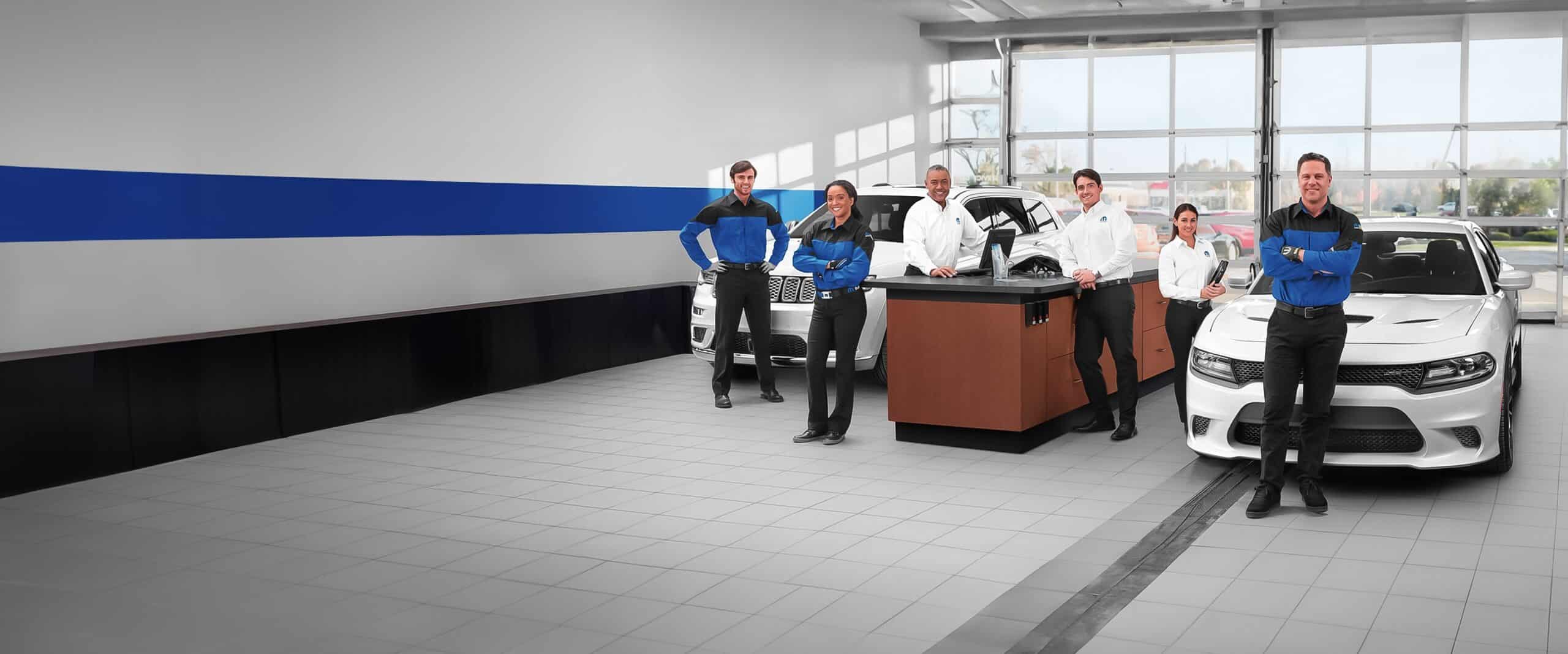 Auto repair team standing in a garage, with cars and tires in the background, smiling confidently.