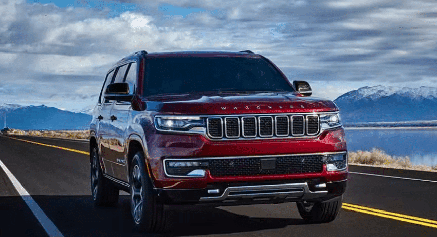 Red SUV driving on an open road with mountains and cloudy sky in the background.