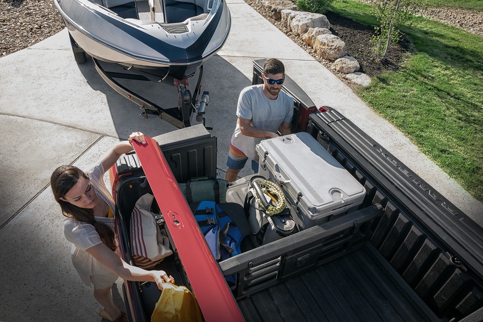 Un homme et une femme chargent une camionnette avec une glacière et des sacs près d'un bateau.