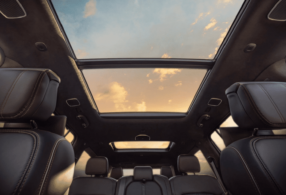 Intérieur avec sièges en cuir et toit ouvrant panoramique montrant un coucher de soleil.