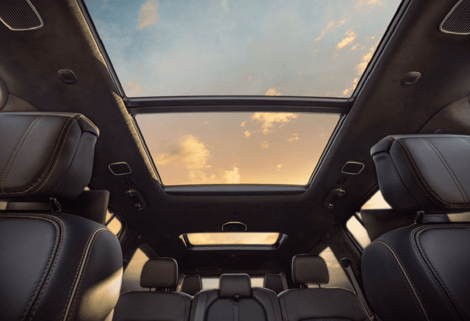 Car interior with leather seats and panoramic sunroof showing a vibrant sunset sky.