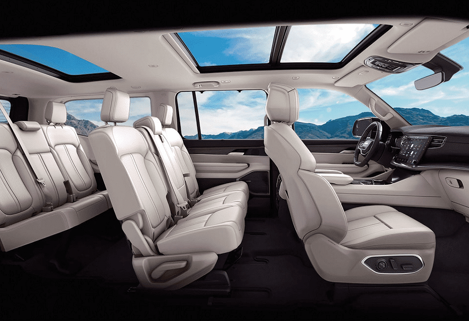 Luxurious car interior with spacious white leather seats and panoramic sunroof, overlooking a mountain view.
