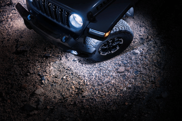 Off-road vehicle with headlights illuminating a rocky terrain at night.