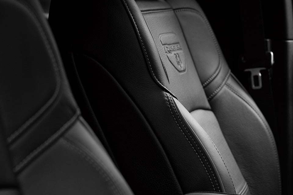 Close-up of a black leather car seat with detailed stitching and the "Rebel" logo embossed.