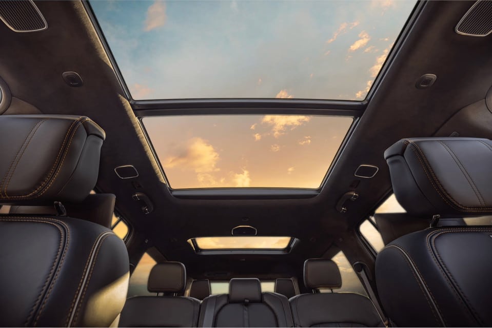 Intérieur avec toit ouvrant panoramique montrant un ciel de coucher de soleil, sièges en cuir.