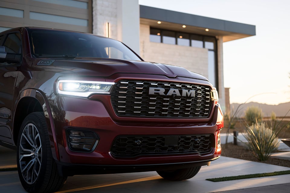 Une camionnette RAM rouge stationnée devant une maison moderne au coucher du soleil.