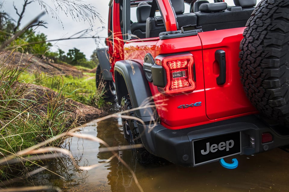 Jeep Wrangler 4xe rouge naviguant un sentier boueux, démontrant sa durabilité et sa capacité hors route.