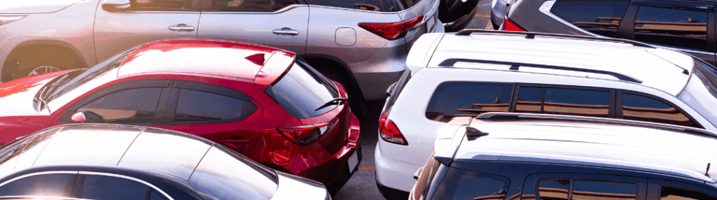 Cars tightly parked in a crowded parking lot, featuring red, white, and silver vehicles.