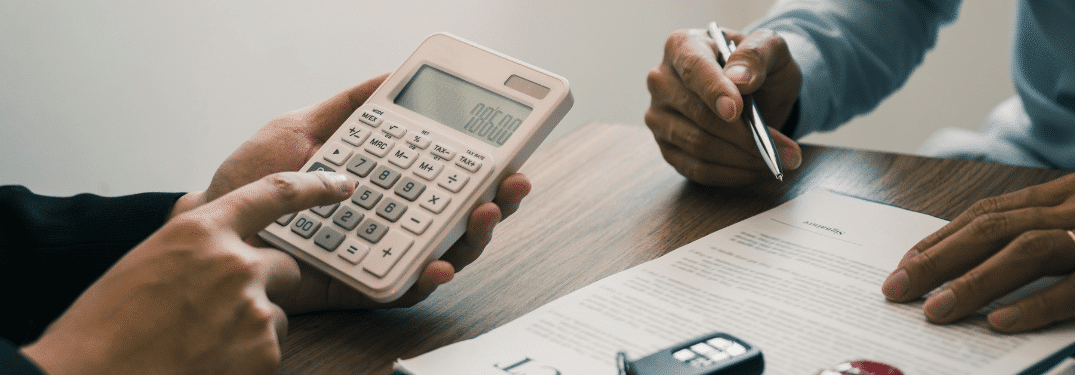 Two people discussing a document at a table, using a calculator and a pen.