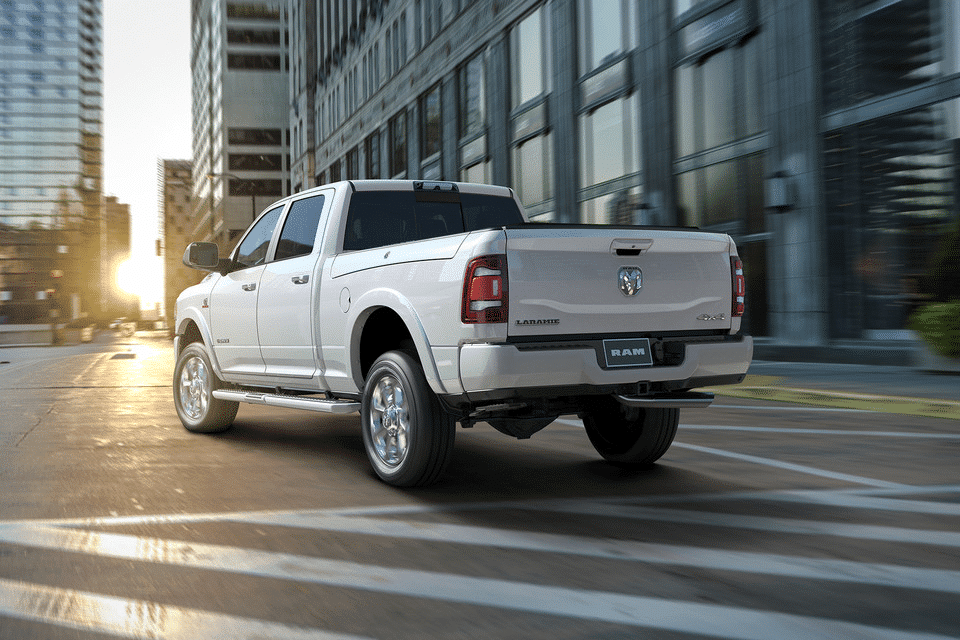 White pickup truck driving on an urban street at sunset, showcasing city buildings and modern design.