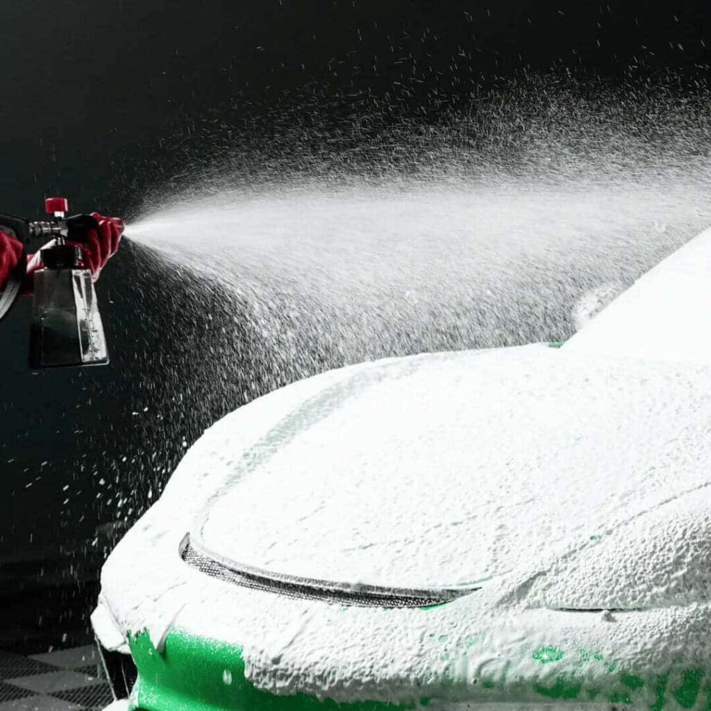 Application de mousse sur une voiture avec un vaporisateur, mettant en valeur le processus de nettoyage détaillé et de nettoyage automatique.
