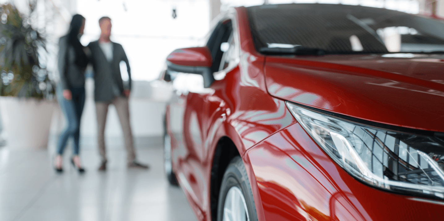 Gros plan d'une voiture rouge en salle d'exposition, couple flou en arrière-plan.