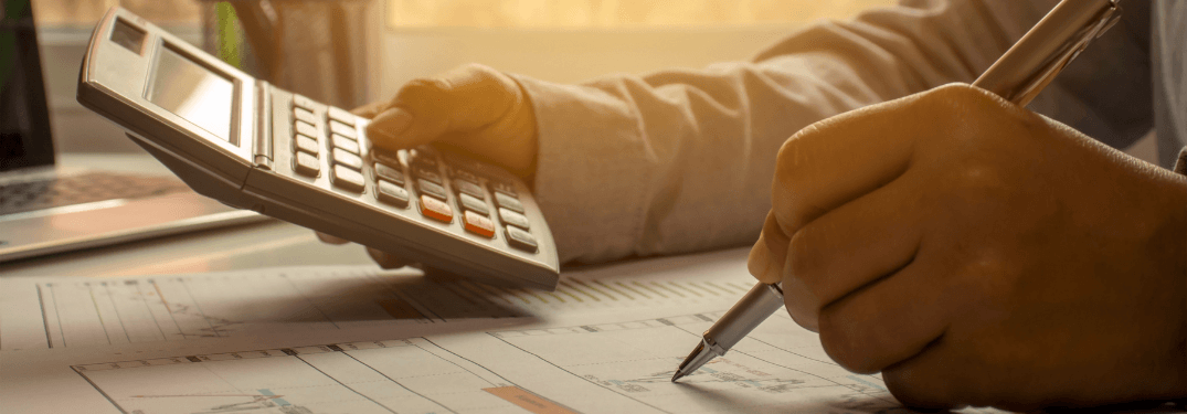 Personne utilisant une calculatrice et un stylo sur des documents financiers, mettant en valeur des calculs d'affaires.