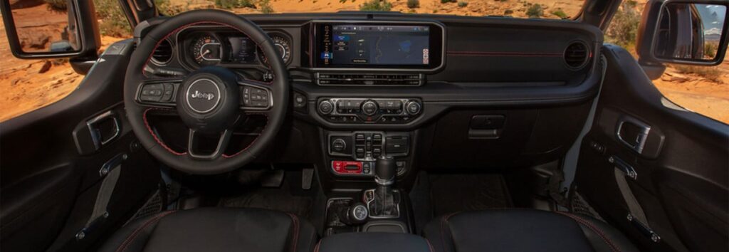 Jeep interior view highlighting steering wheel, dashboard, touchscreen, and control panel in a rugged landscape.