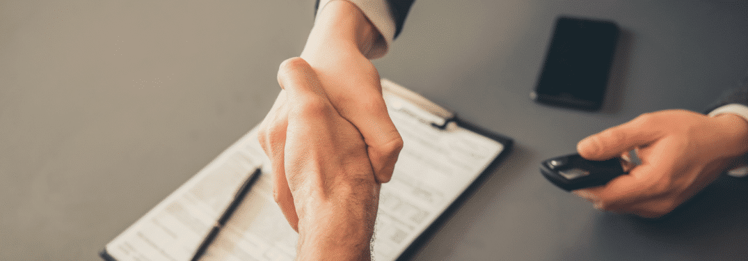 Poignée de main au-dessus de documents contractuels, avec un téléphone intelligent et une clé de voiture en arrière-plan, symbolisant un accord.