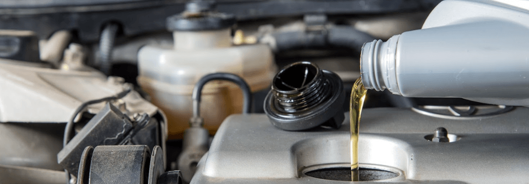 Pouring engine oil into a car engine in a maintenance setting.