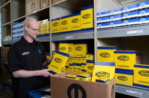 Un employé organise des boîtes Magneti Marelli sur des étagères dans un entrepôt, démontrant une gestion efficace des stocks.