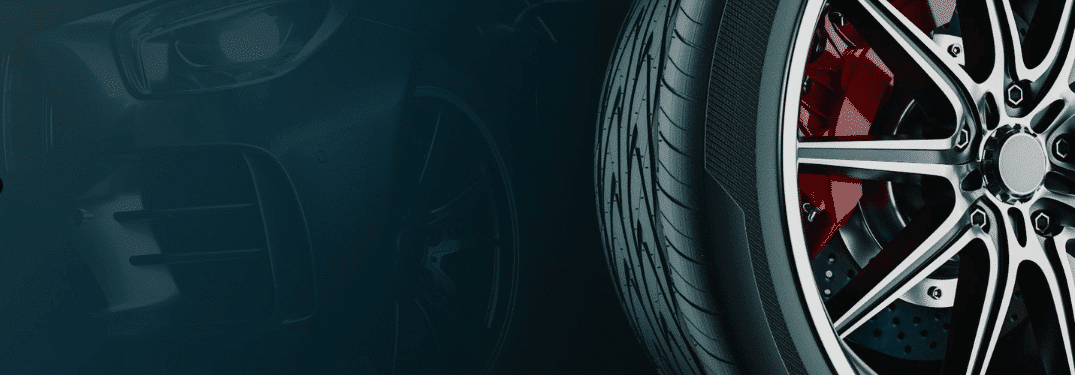 Close-up of a car tire with shiny alloy wheel, brake disc, and part of vehicle front.