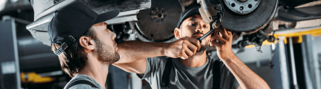 Deux mécaniciens en uniforme travaillant sous une voiture, concentrés sur les réparations et l'entretien.