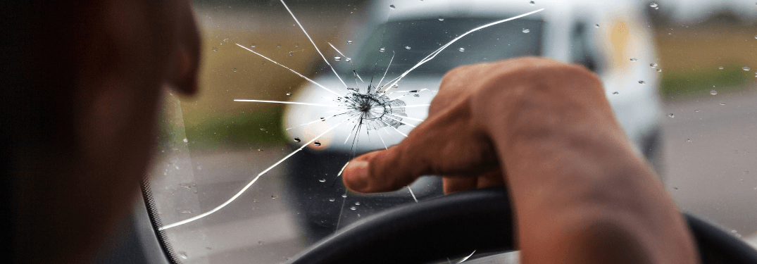 Un conducteur pointe un pare-brise fissuré en conduisant sur la route.