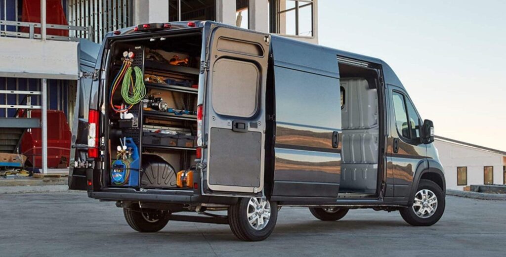 Utility van with open doors showing organized tools and equipment, parked near a building.