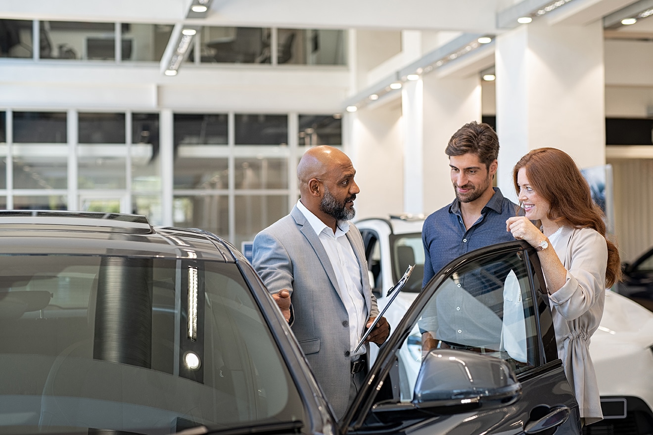Couple discutant avec un vendeur dans une concession automobile, examinant un nouveau véhicule.