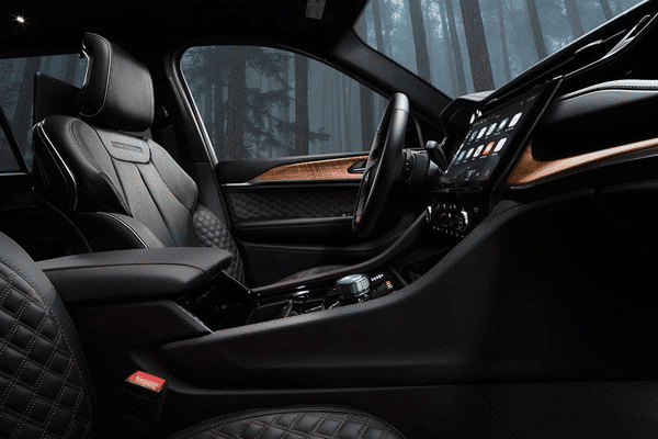 Luxurious car interior with leather seats, high-tech dashboard, and wooded accents against a forest background.