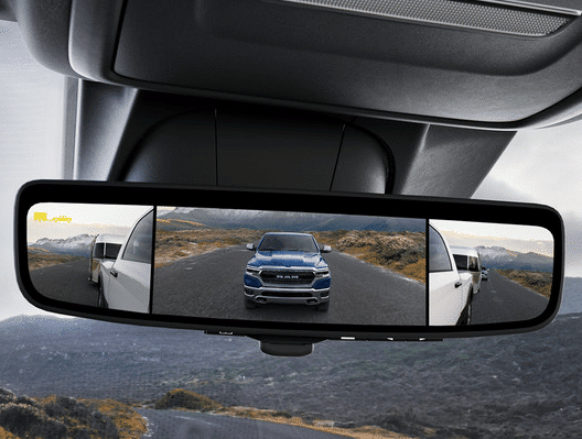 Rearview mirror displaying a split-camera view of a vehicle towing a trailer on a scenic road.