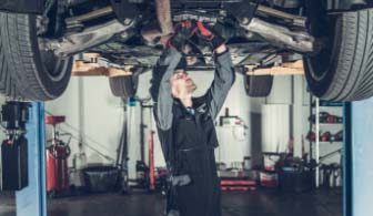 Mechanic in a workshop working under a lifted car, inspecting and repairing the vehicle.
