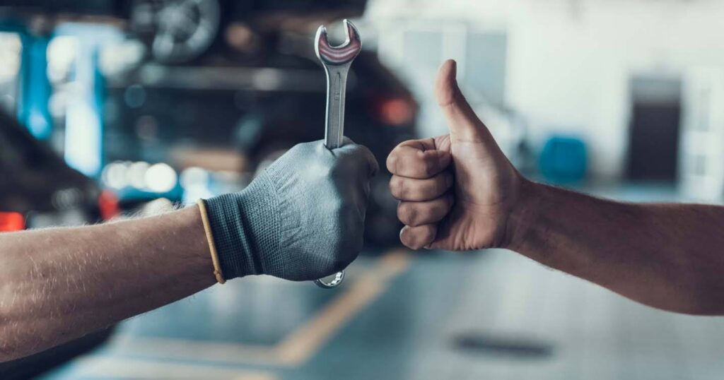 Mechanic's gloved hand holding a wrench, with another hand showing a thumbs-up gesture.