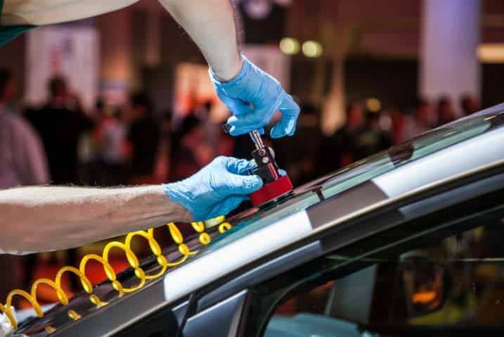 Technician repairing car windshield with a suction tool, wearing blue gloves.