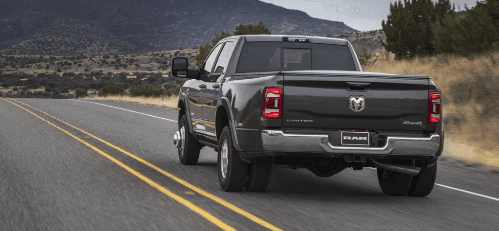 A black Ram 4x4 pickup truck driving on a scenic country road with mountains.