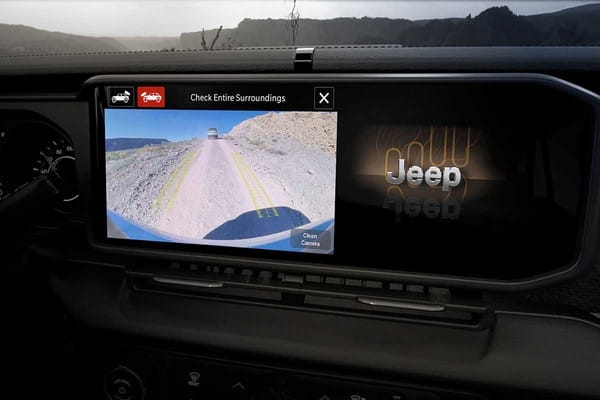 Tableau de bord d'un Jeep affichant un écran de caméra de recul montrant un chemin accidenté, avec un logo Jeep numérique à droite.