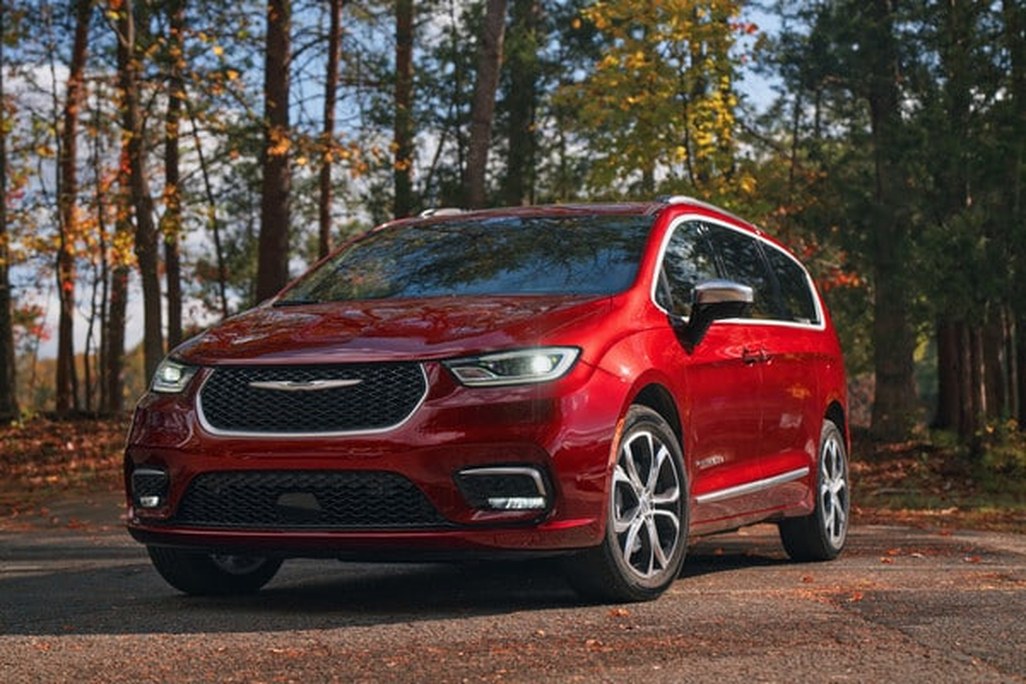 Red Chrysler minivan in autumn forest setting, highlighting sleek design and fall colors.