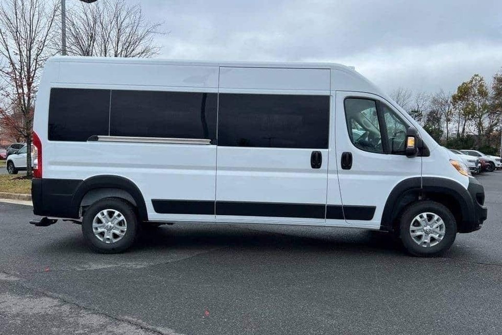 White passenger van parked on an asphalt lot, trees and cloudy sky in the background.